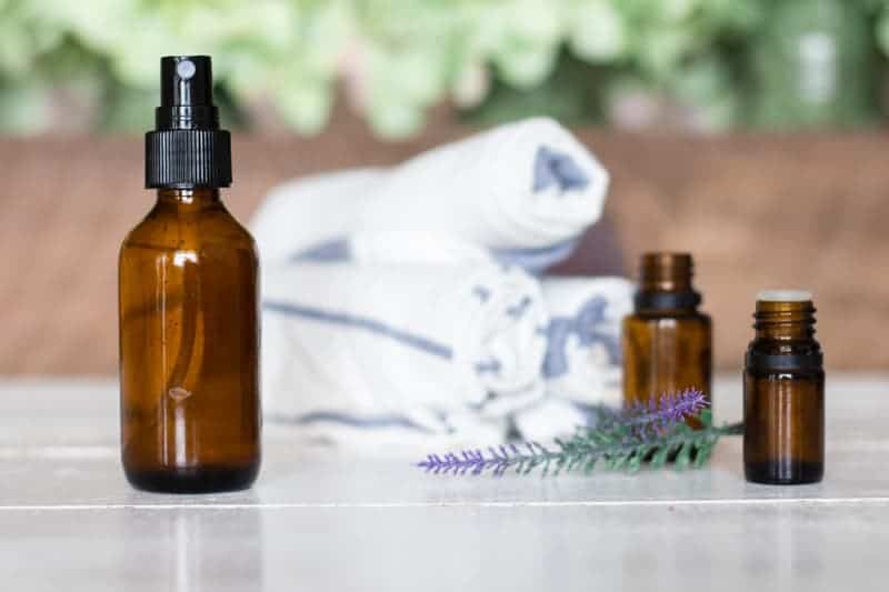 Amber glass spray bottle with white towels and essential oil bottles in background.