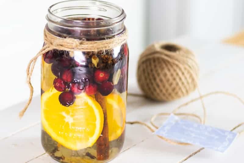 Cranberries, orange slices, fresh herbs, and cinnamon sticks in mason jar on shiplap.