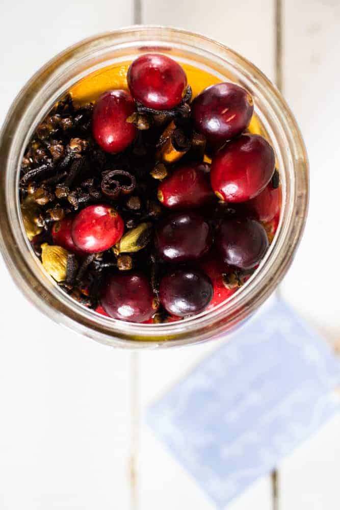 Mason jar full of cranberries, cloves, and orange slices.