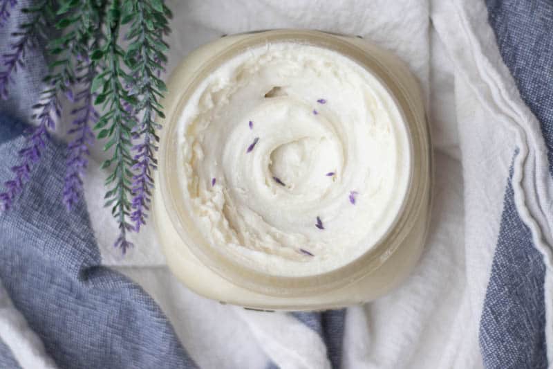 Lavender lotion in mason jar on white and blue towel with lavender sprigs.