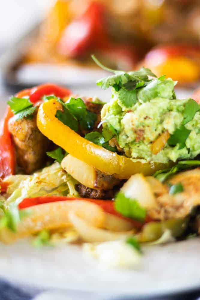 Bell peppers, chicken, homemade guacamole and cilantro on white plate.