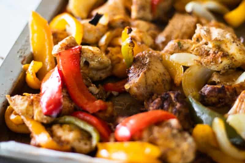 Chicken fajita sheet pan with bell peppers, onions and homemade seasoning on baking dish.