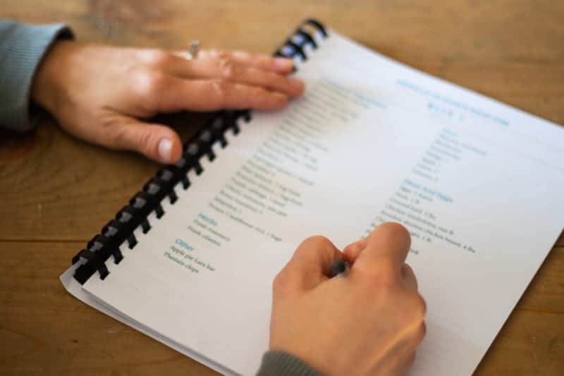 Filling out grocery list for whole 30 meal planning on wooden table.