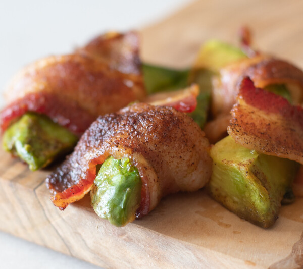 bacon wrapped avocado fries on wood board.