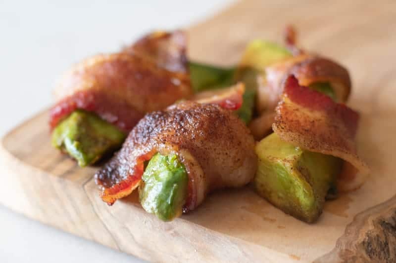 Bacon wrapped avocado fries on wood cutting board.