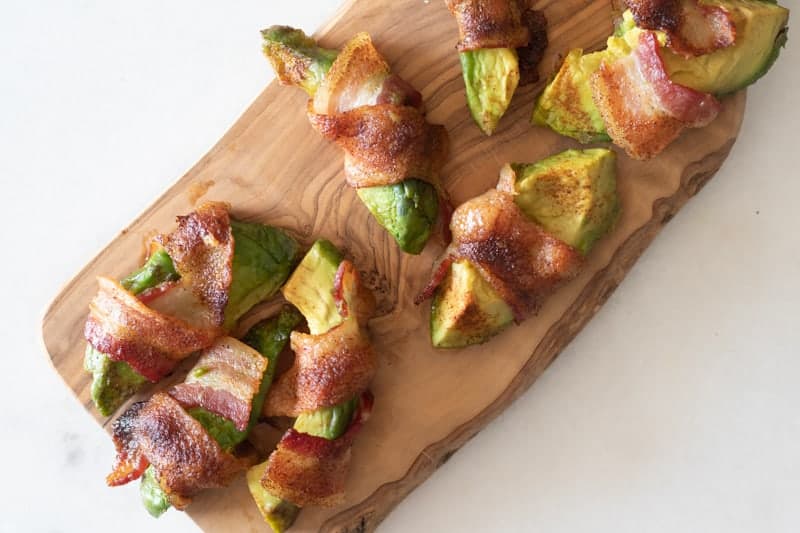 Bacon wrapped avocado fries on wood cutting board.