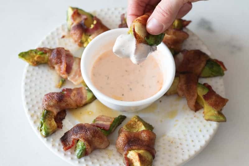 Bacon wrapped avocado fry being dipped in spicy paleo dip.