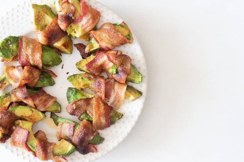 Avocado wrapped in bacon on white plate over white background.