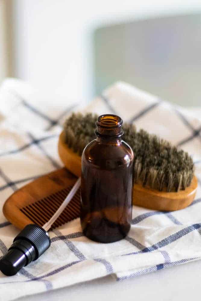 Homemade aftershave in amber glass spray bottle with a wooden beard comb and brush.