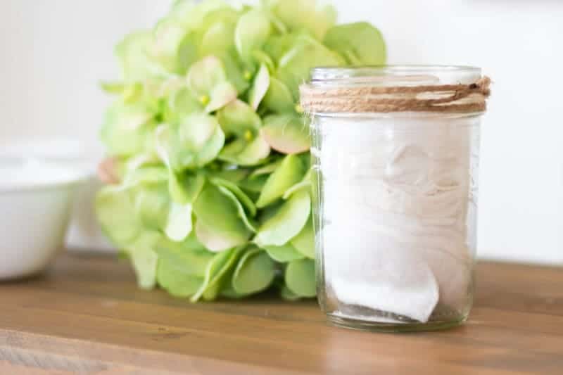 Homemade makeup remover cloths in mason with green flower in background.