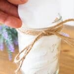 hnad holding white cotton round over small mason jar of makeup remover