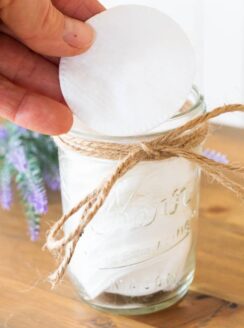 hnad holding white cotton round over small mason jar of makeup remover