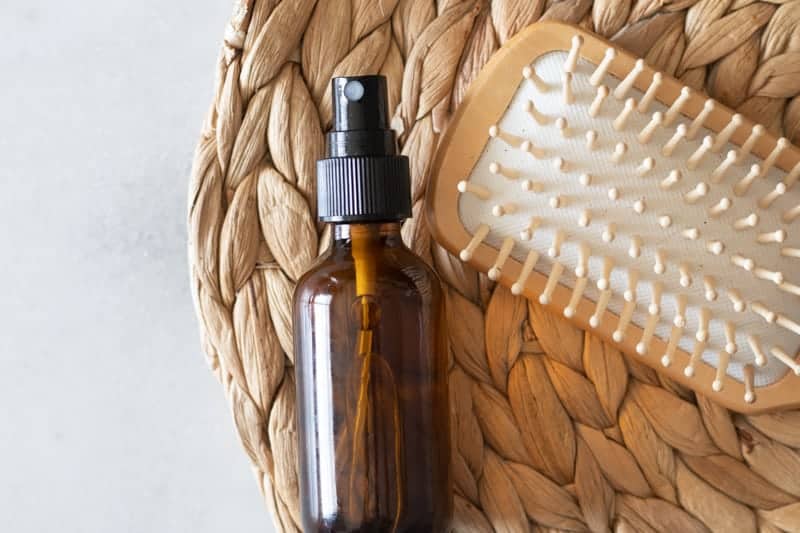 Amber glass spray bottle and tan brush on wicker place mat.