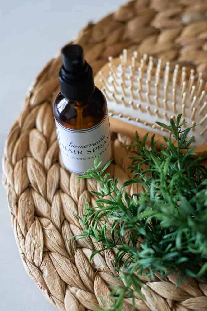 Hair spray in glass bottle and hair brush on wicker placemat.