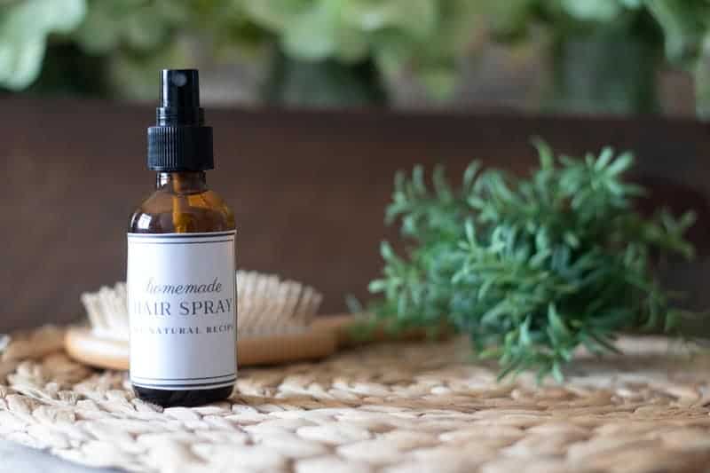 DIY hair spray bottle with white label with greenery in background.