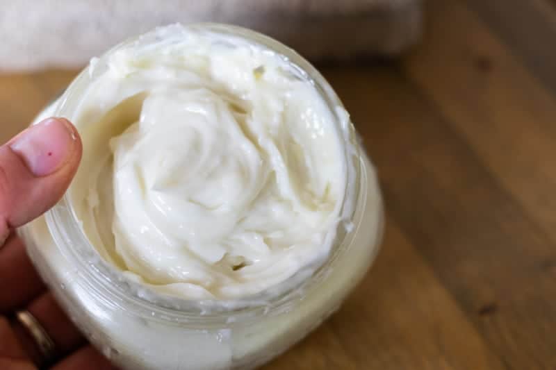 Hand holding fluffy white shaving cream in mason jar over wooden table.