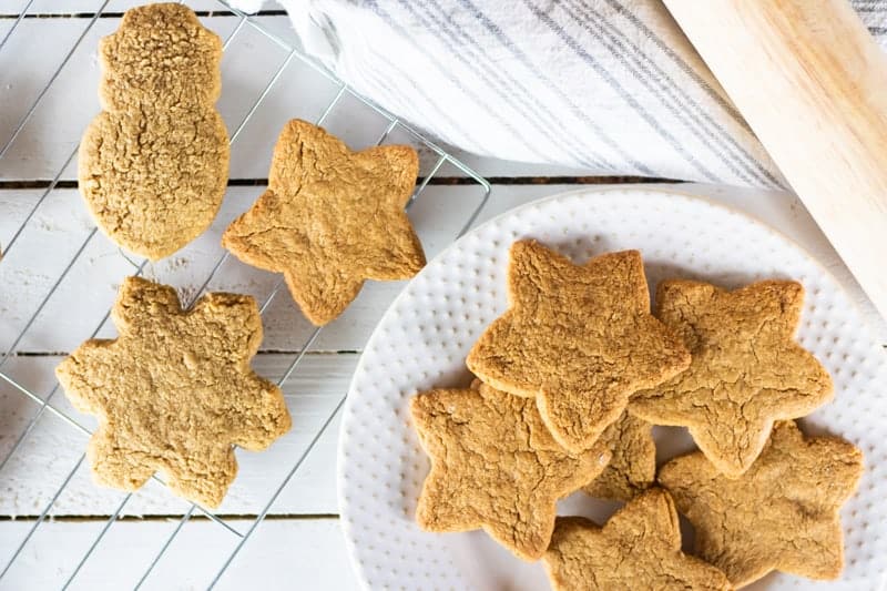 Cutout Christmas sugar cookies on cooling rack and on white plate.