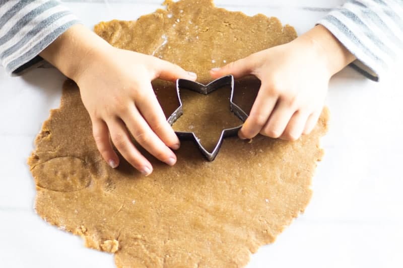 Hands pressing star shaped cookie cutter into rolled out dough.