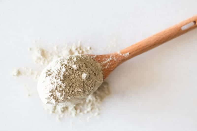 bentonite clay on wooden spoon on a marble counter.