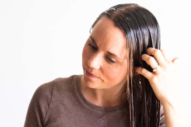 Woman applying hair mask to long brown hair.