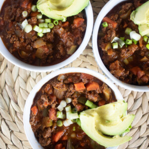 Three bowls of whole30 chili topped with avocado slices and green onions.