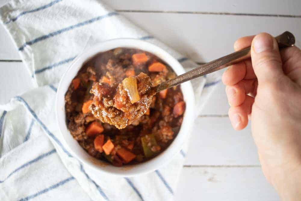 hand using spoon to take a bite of chili