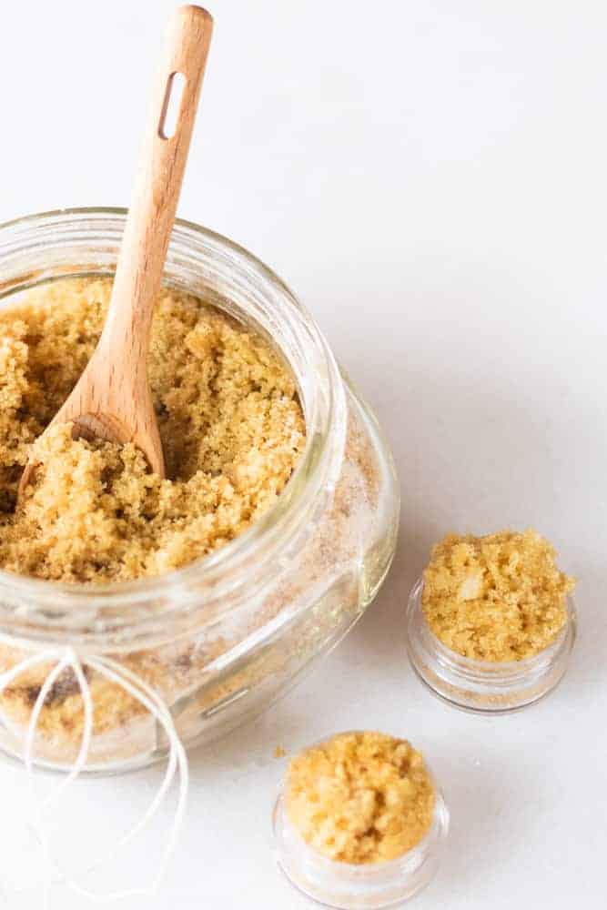 Lip exfoliator with a wooden scooping spoon in a small glass jar.
