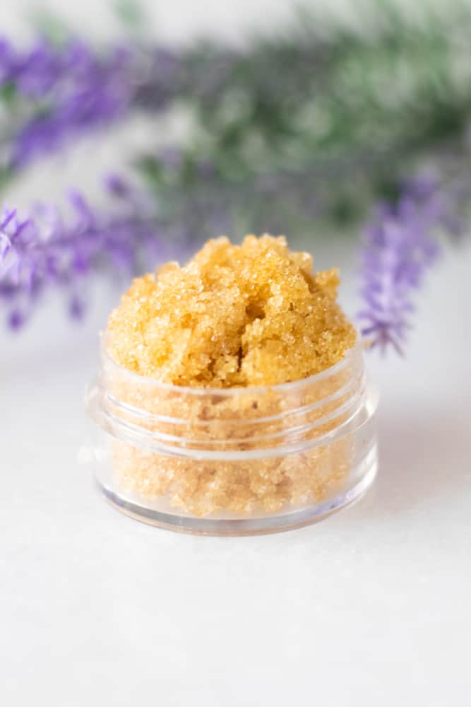 lavender lip scrub in small container with lavender flowers on white marble table top