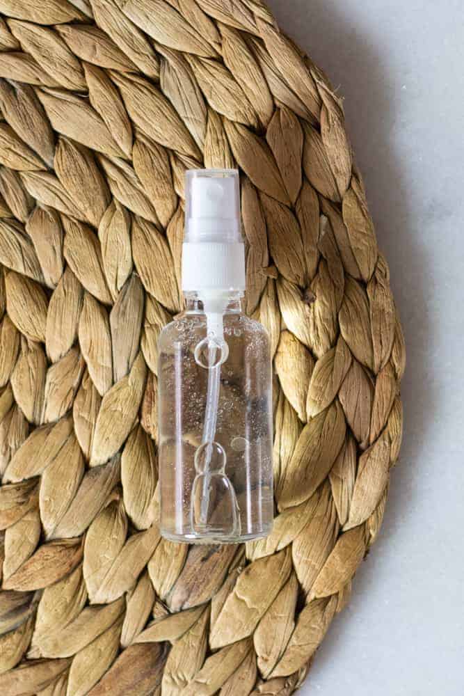 clear spray bottle with hair growth spray on a woven bamboo mat