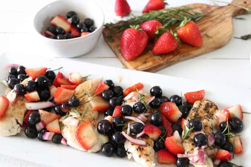 grilled chicken with berry salsa on white plate on white shiplap. 