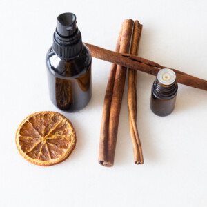 amber glass bottle. cinnamon sticks, orange slice, and essential oils on white marble