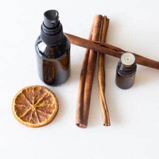 amber glass bottle. cinnamon sticks, orange slice, and essential oils on white marble