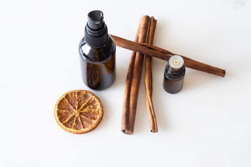 amber glass bottle. cinnamon sticks, orange slice, and essential oils on white marble