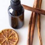 diy hand sanitizer spray in glass bottle with cinnamon sticks and orange slices on white table