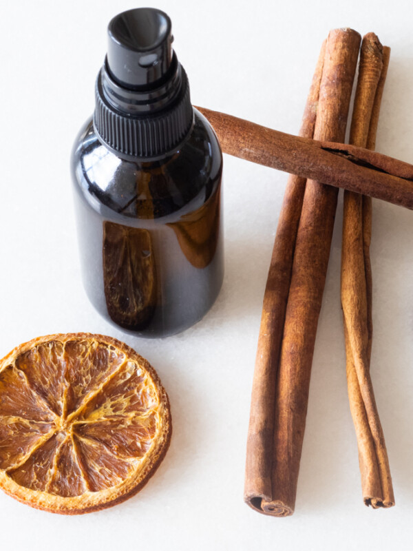 diy hand sanitizer spray in glass bottle with cinnamon sticks and orange slices on white table