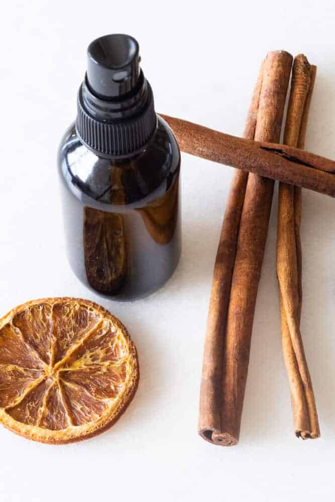 diy hand sanitizer spray in glass bottle with cinnamon sticks and orange slices on white table