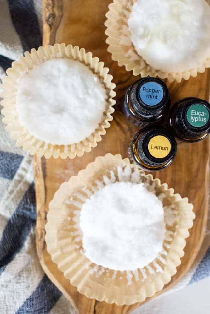 essential oil bottle by baking soda shower disks on wood cutting board