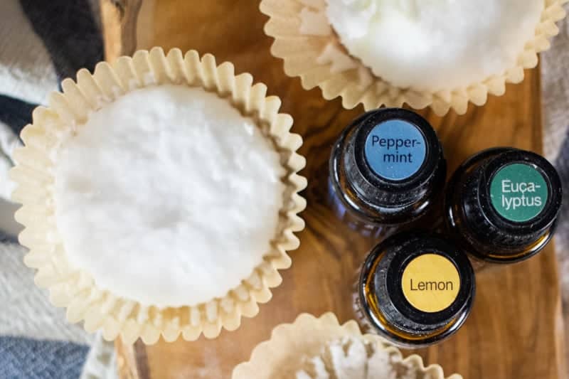 diy shower disk in cupcake liner and essential oil bottles on wood cutting board