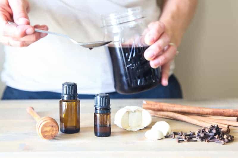 essential oil bottles, garlic, cinnamon sticks, and mason jar of elderberry syrup on table