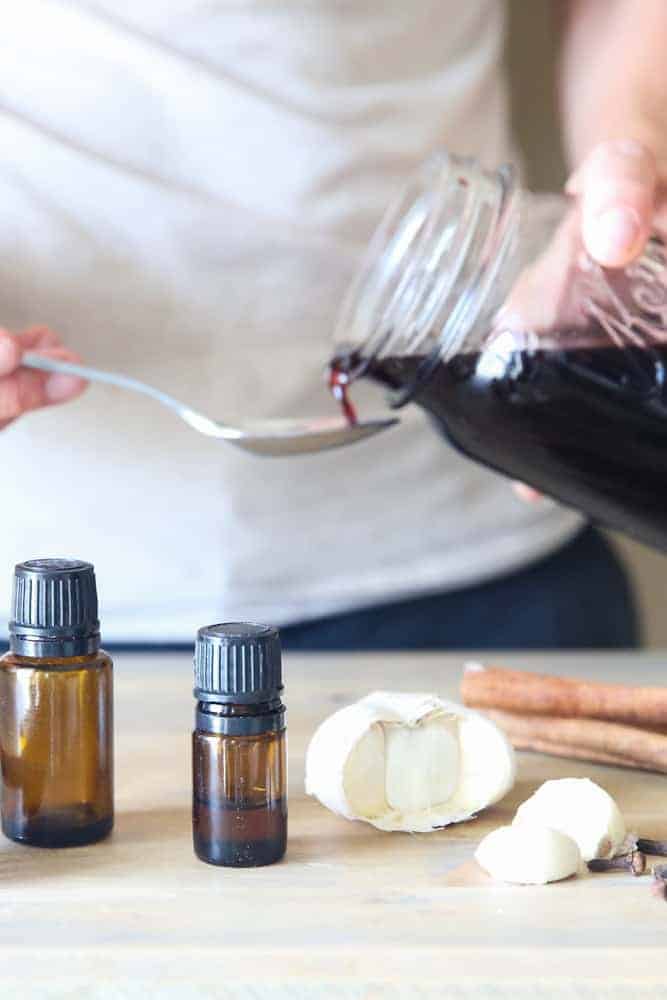 pouring homemade elderberry syrup out of mason jar onto spoon