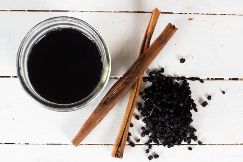 elderberry syrup in mason jar on white shiplap with dried elderberries and cinnamon sticks