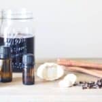 mason jar of elderberry syrup, garlic cloves, and essential oils on table