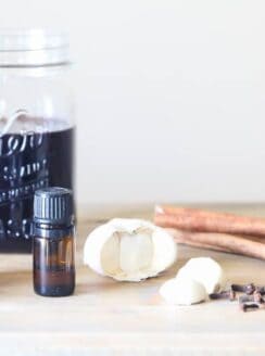 mason jar of elderberry syrup, garlic cloves, and essential oils on table