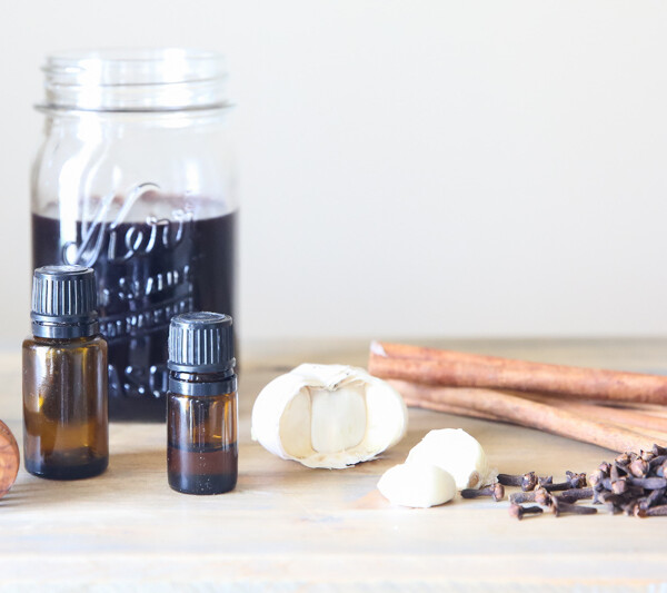 mason jar of elderberry syrup, garlic cloves, and essential oils on table