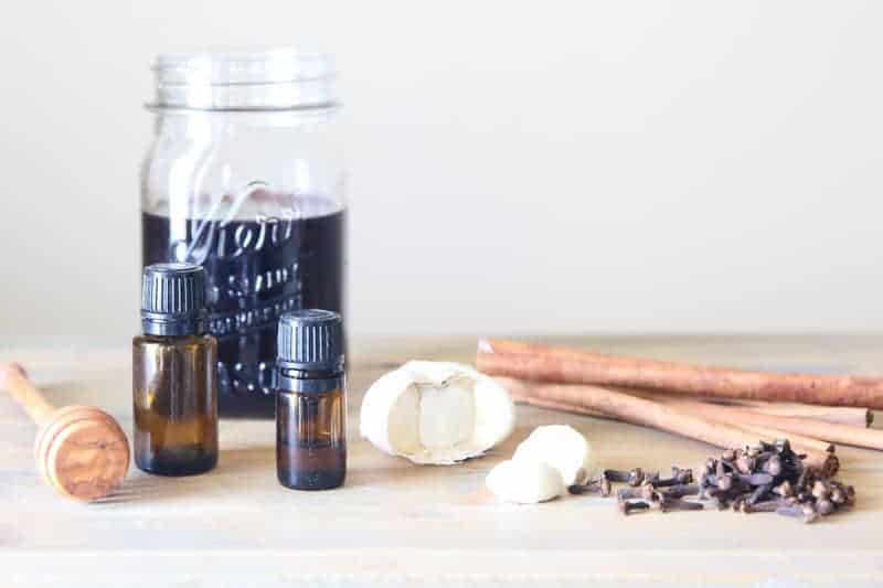 mason jar of elderberry syrup, garlic cloves, and essential oils on table