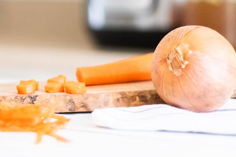 sliced carrots and whole onion on wooden cutting board