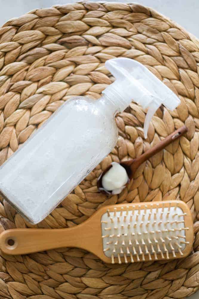 glass spray bottle with heat protection spray next to a brush and tablespoon on round woven mat