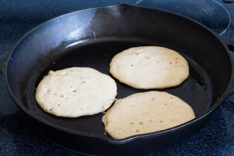 sourdough pancake batter frying in cast iron skillet
