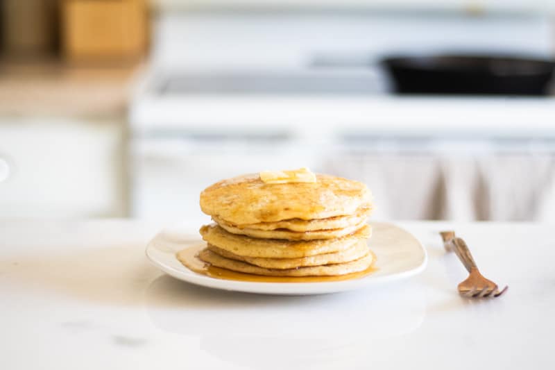 stack of pancakes on white marble counter with brass fork