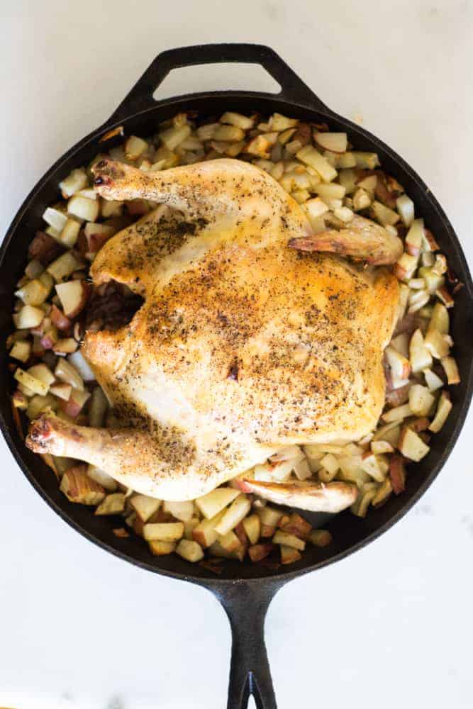 roasted whole chicken and red potatoes in cast-iron skillet on white marble